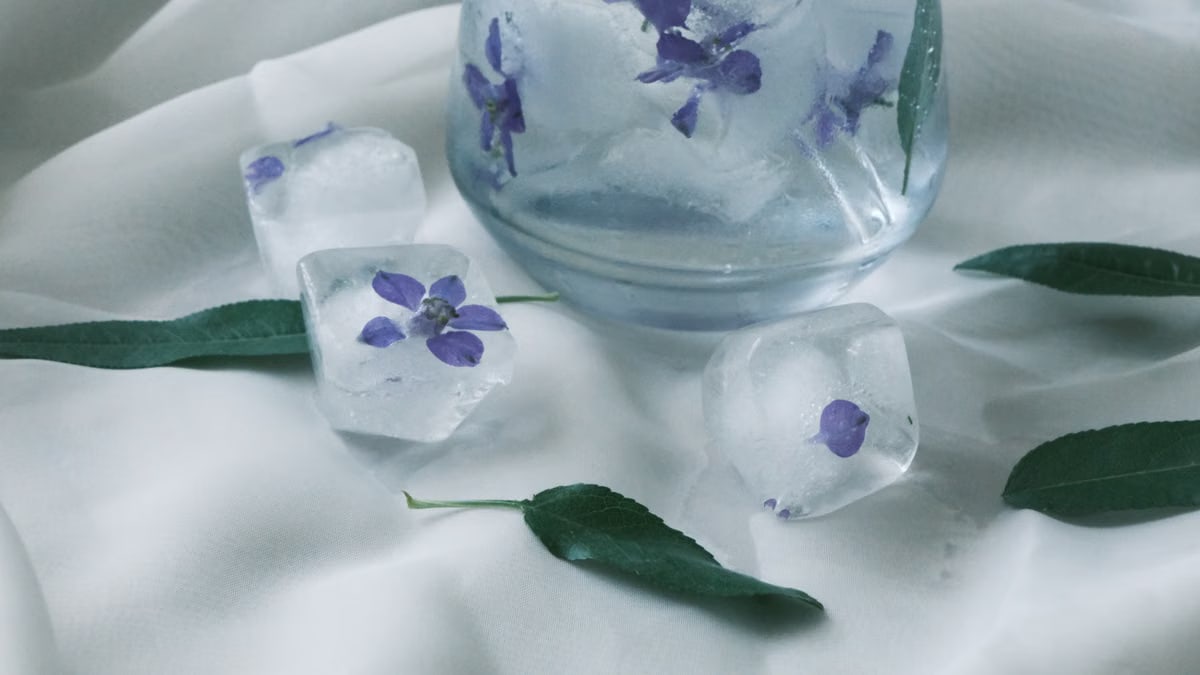 Artistic arrangement of ice cubes with purple flowers and green leaves on a white background.